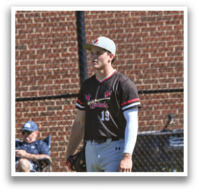 A baseball player in a red shirt and white pants is standing on a field. Description generated by AI
