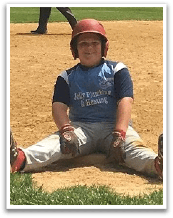 A young boy wearing a baseball uniform is sitting on the ground with his legs spread out. AI generated content