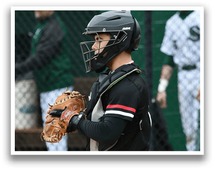 A baseball catcher in a black shirt and white pants with a baseball glove. Description generated by AI
