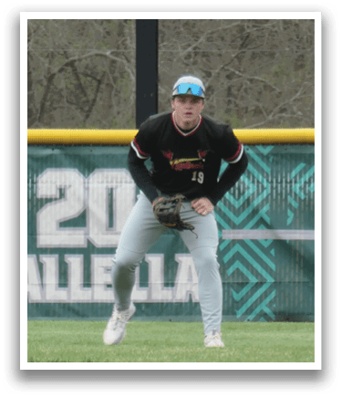 A baseball player wearing a black shirt and grey pants is standing on the field. Description generated by AI