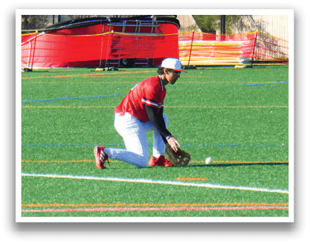 A man wearing a red shirt is kneeling on a grass field. Description generated by AI