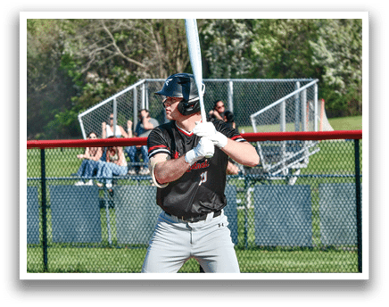 A baseball player in a black shirt and grey pants holding a bat. Description generated by AI