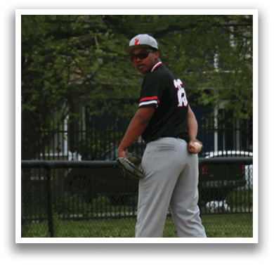 A baseball player in a black shirt and grey pants is standing on a mound. Description generated by AI