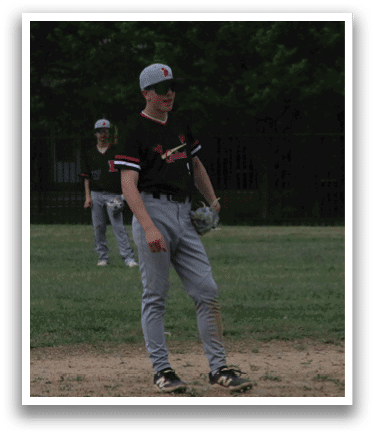 A boy wearing a baseball uniform stands on a baseball field. Description generated by AI