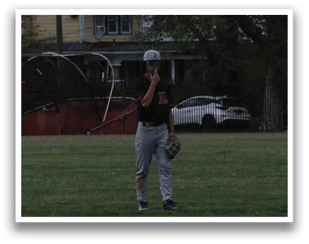 A baseball player in a black and red shirt and grey pants standing on a field. Description generated by AI