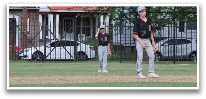 A boy in a baseball uniform stands on a baseball field. Description generated by AI