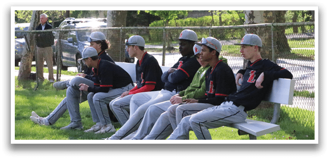 A group of young men wearing baseball caps and jerseys are sitting on a bench. Description generated by AI