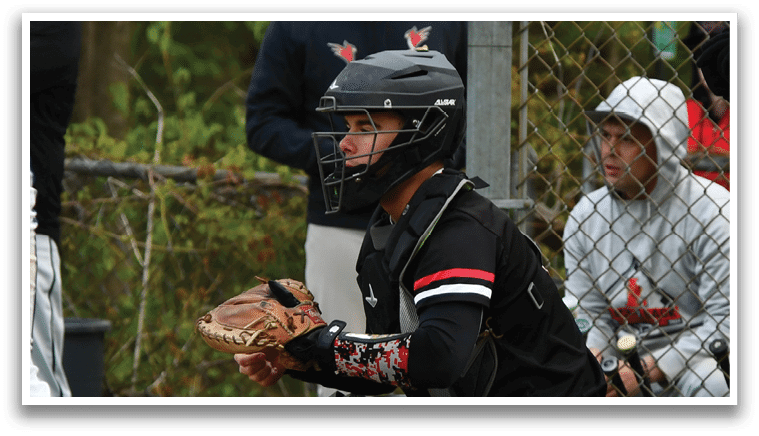 A baseball player in a black and red uniform squatting on the field. Description generated by AI