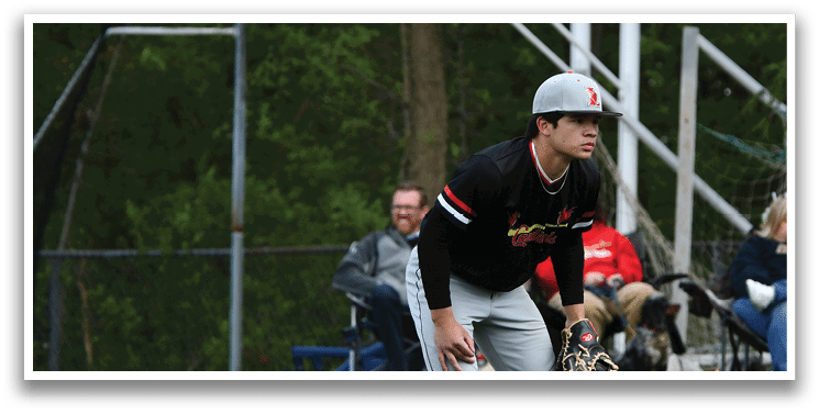 A baseball player in a black shirt and grey pants is crouching on the field. Description generated by AI