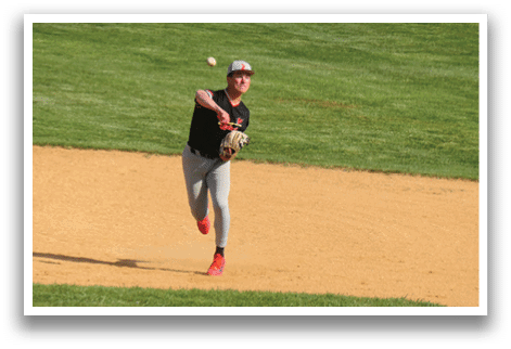 A baseball player in a black shirt and red shoes is throwing a ball. Description generated by AI