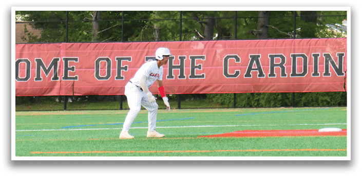 A baseball game is taking place on a field with a red and white banner. Description generated by AI