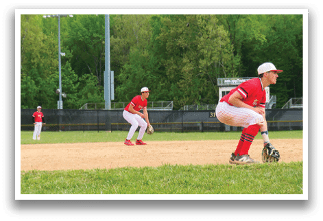 A baseball player in a red shirt and white pants is crouching on the field. Description generated by AI