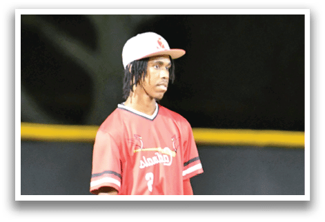 A young man wearing a red shirt and white pants stands on a baseball field. Description generated by AI