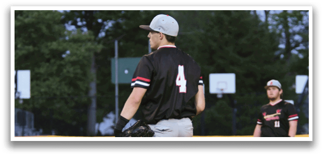 A baseball player wearing a black shirt and white pants stands on the pitcher's mound. Description generated by AI