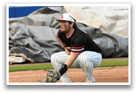 A baseball player in a black and red uniform crouches on the field. Description generated by AI