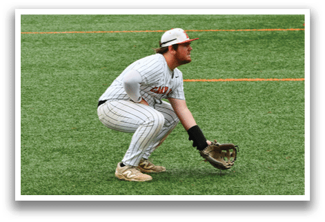 A baseball player in a white and orange uniform is kneeling on the field. Description generated by AI