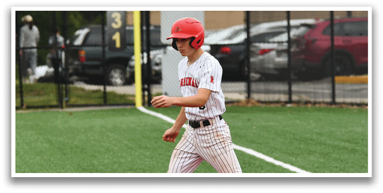 A boy wearing a red helmet and white and red uniform is walking on a baseball field. Description generated by AI