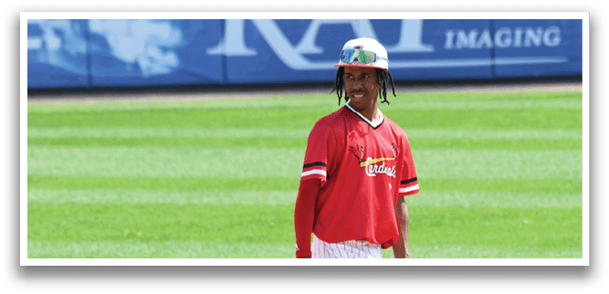 A man wearing a red shirt and white pants is walking on a baseball field. Description generated by AI