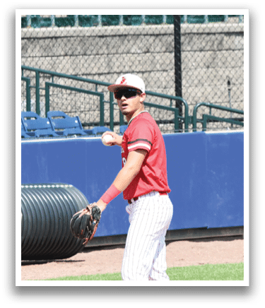 A baseball player in a red shirt and white pants is standing on a baseball field. Description generated by AI