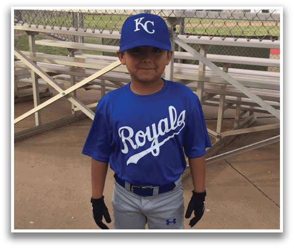 A young boy wearing a blue baseball uniform stands on a baseball field. AI generated content