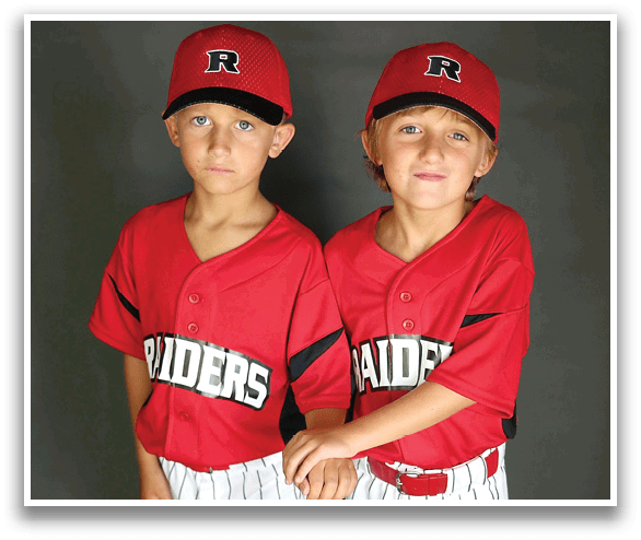 Two young boys wearing red and white baseball uniforms are standing next to each other and holding baseball bats. AI generated content