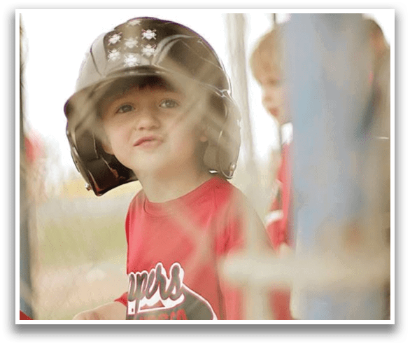 A young boy wearing a baseball helmet and a red shirt is sitting in the dugout. AI generated content