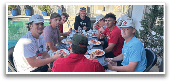 A group of young men are sitting around a table, enjoying a meal together. AI generated content