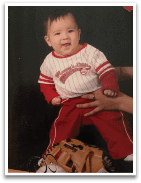 A baby wearing a baseball jersey is standing next to a baseball bat. AI generated content