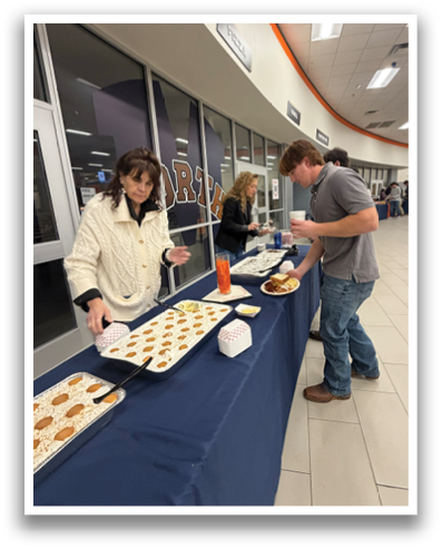 People are gathered around a table with food and drinks. A man is serving food to a woman. There are several chairs around the table. Contenido generado con IA