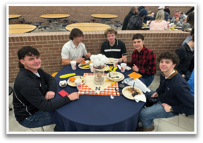 A group of people are sitting around a table with plates of food, cups, and a vase of flowers. They are enjoying a meal together. Contenido generado con IA