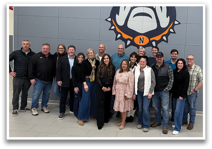 A group of people posing for a photo in front of a wall with a bulldog mascot. Contenido generado con IA