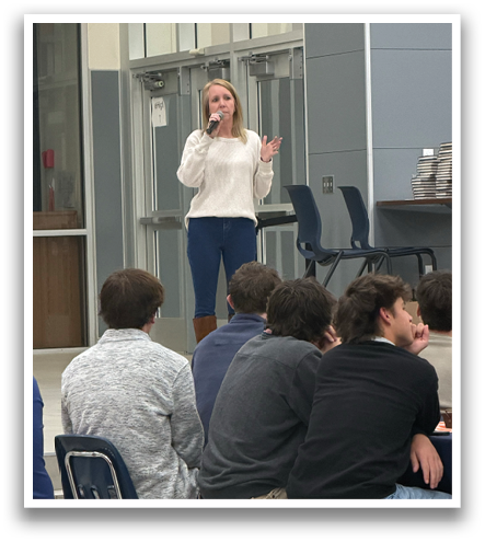 A woman is standing in front of a group of people, speaking into a microphone. Contenido generado con IA