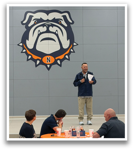A man is standing in front of a group of people at a table. Contenido generado con IA