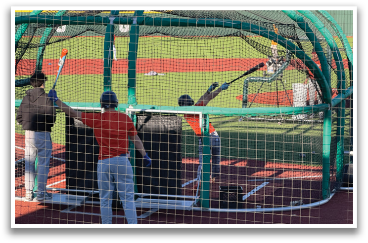 A group of people are standing in a batting cage, holding baseball bats and preparing to hit the ball. Contenido generado con IA