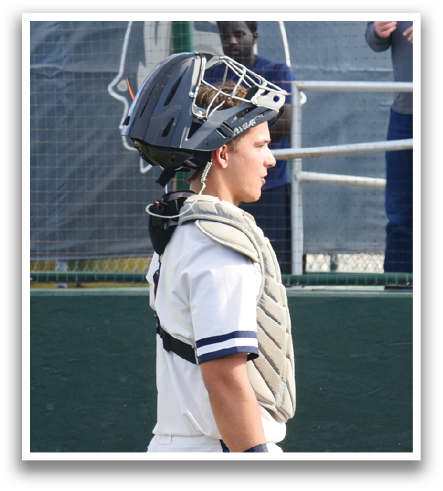 A baseball player wearing a helmet and catcher's gear is standing on the field. Contenido generado con IA