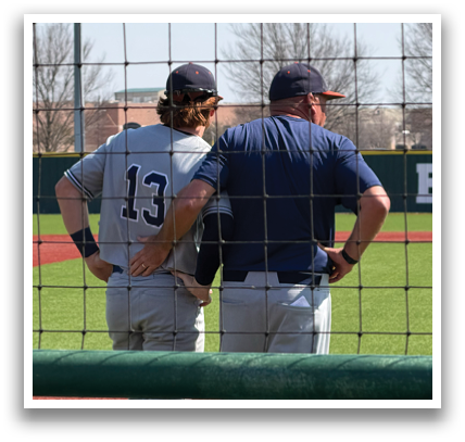 Two men are standing on a baseball field, talking to each other. One of them is wearing a baseball uniform. Contenido generado con IA
