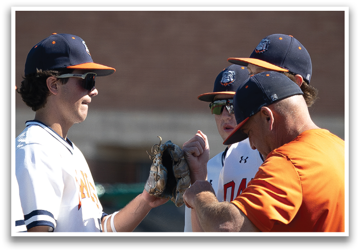 Three baseball players wearing orange and white uniforms are standing on a field. They are talking to each other and one of them is holding a baseball glove. Contenido generado con IA