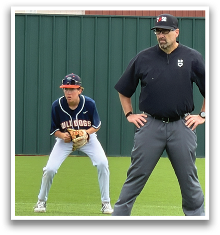 Two men are playing baseball on a field. One man is wearing a blue shirt and is holding a baseball glove. The other man is wearing a black shirt and is watching the game. Contenido generado con IA