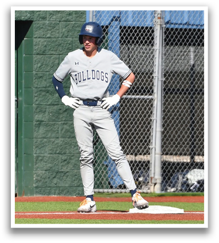 A baseball player wearing a blue helmet and white uniform is standing on a baseball field. Contenido generado con IA