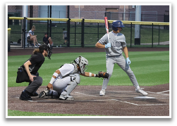 A baseball game is taking place with a batter holding a bat, ready to swing. The catcher is positioned behind the batter, wearing a baseball glove. There are several other people in the scene, likely teammates and opponents. The game is being played on a baseball field, with a car visible in the background. Contenido generado con IA