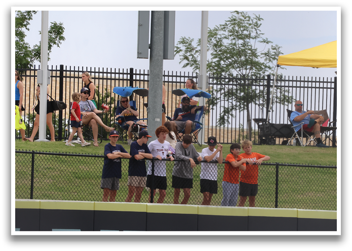 A group of people are sitting on a grassy hill, watching a baseball game. They are sitting on chairs and on the ground, enjoying the outdoor event. Contenido generado con IA