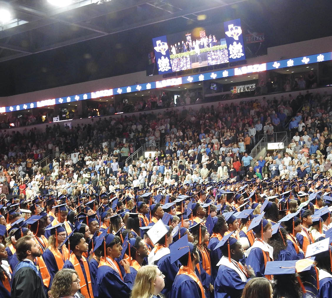 A large group of people wearing blue caps and gowns are sitting in the bleachers. Contenido generado con IA