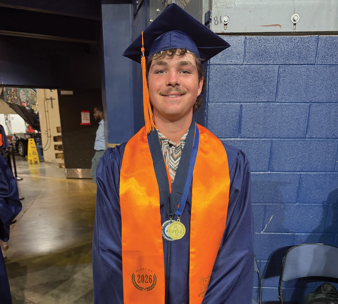 A man wearing a blue gown and an orange sash stands in a room. Contenido generado con IA