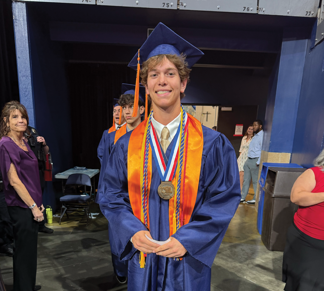 A man wearing a blue graduation robe and holding a medal stands in a hallway. Contenido generado con IA