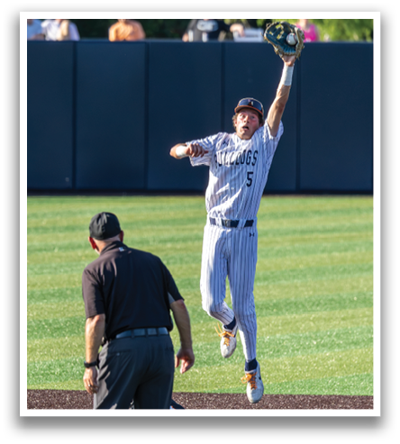 A baseball player jumps in the air to catch a ball while a referee watches. Contenido generado con IA