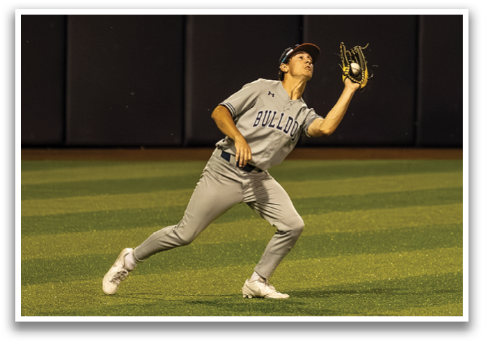 A baseball player in a grey uniform is trying to catch a ball. Contenido generado con IA
