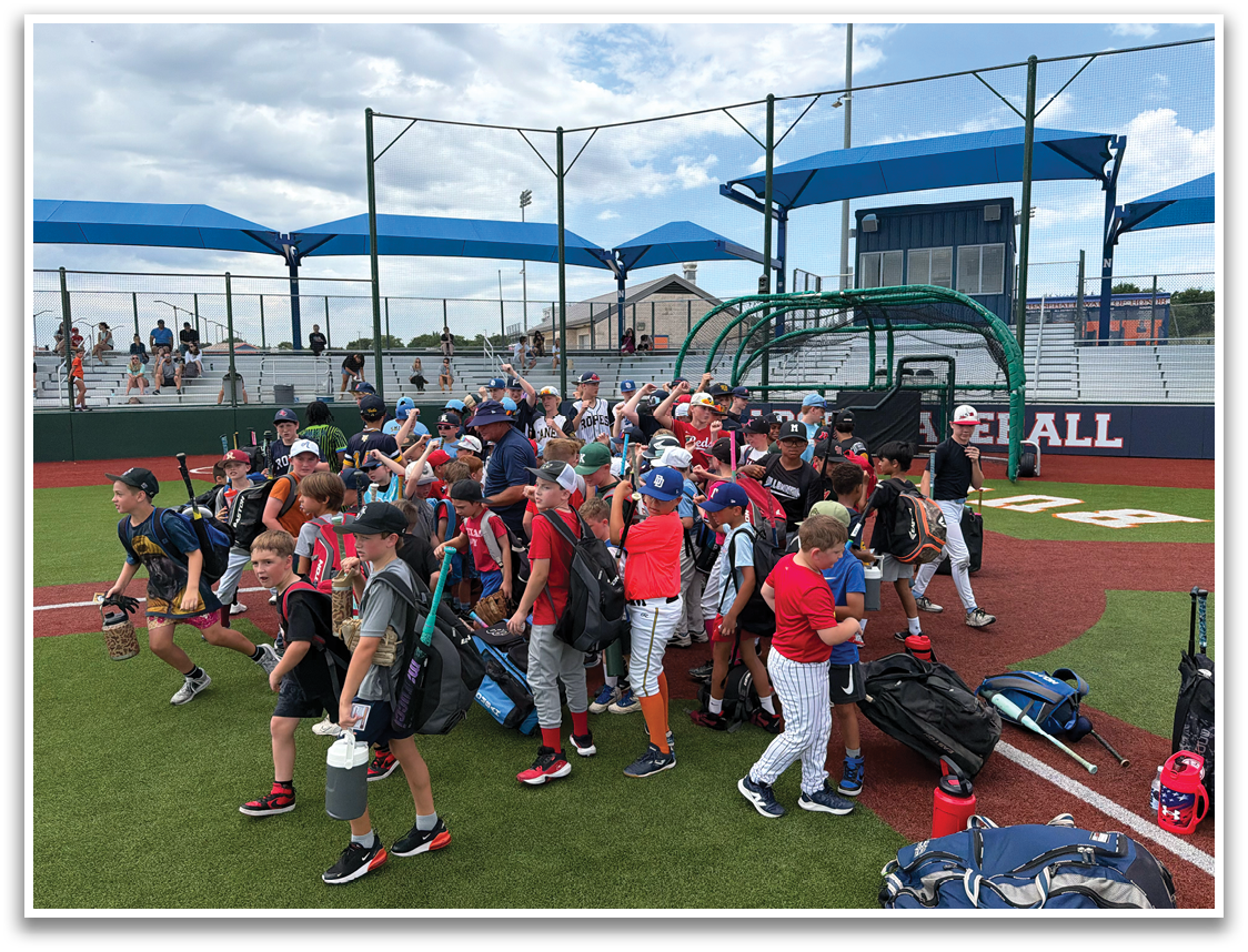 A group of young baseball players are gathered on a baseball field, some carrying bags and equipment. Contenido generado con IA