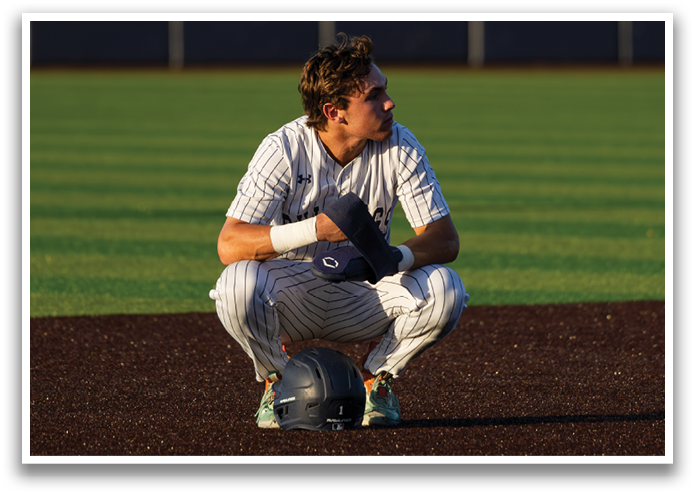 A baseball player is kneeling on the field, wearing a helmet and holding a bat. Contenido generado con IA