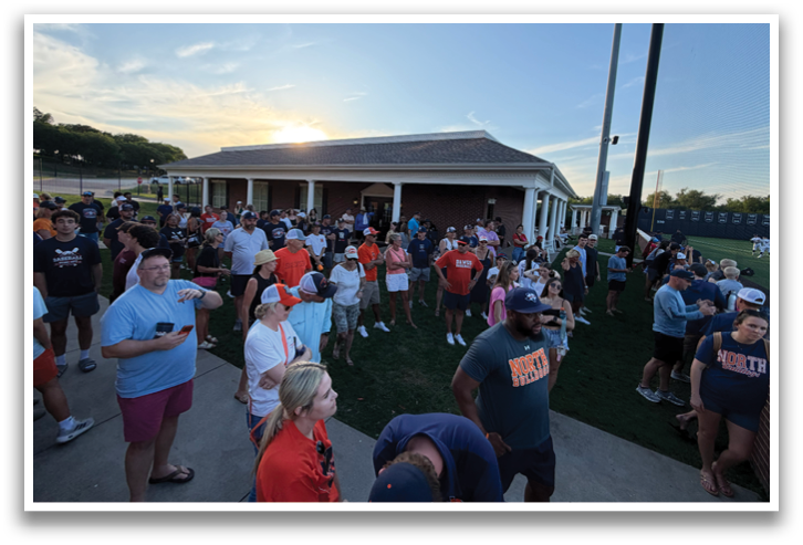 A large crowd of people are gathered outside of a building, with some of them holding cell phones. The group is diverse, with individuals of various ages and genders. The scene appears to be a social event or gathering, with people standing and interacting with one another. Contenido generado con IA