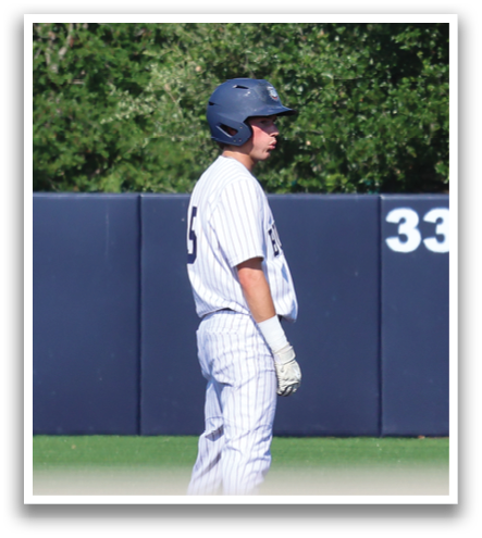 A man stands in front of a baseball field, wearing a baseball uniform and a blue hat. He is looking at a sign on the wall. Contenido generado con IA